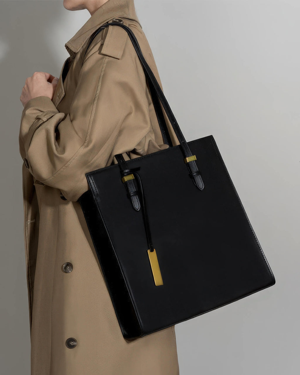 Close-up of a black genuine leather tote bag with gold hardware worn over the shoulder.