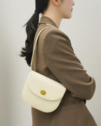 Side three-quarter angle of an off-white classic leather flap saddle crossbody bag worn with a brown blazer.