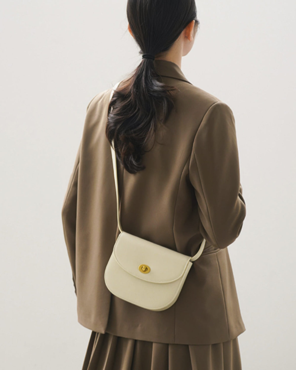 Back view of an off-white classic leather flap saddle crossbody bag worn by a model in a brown blazer.