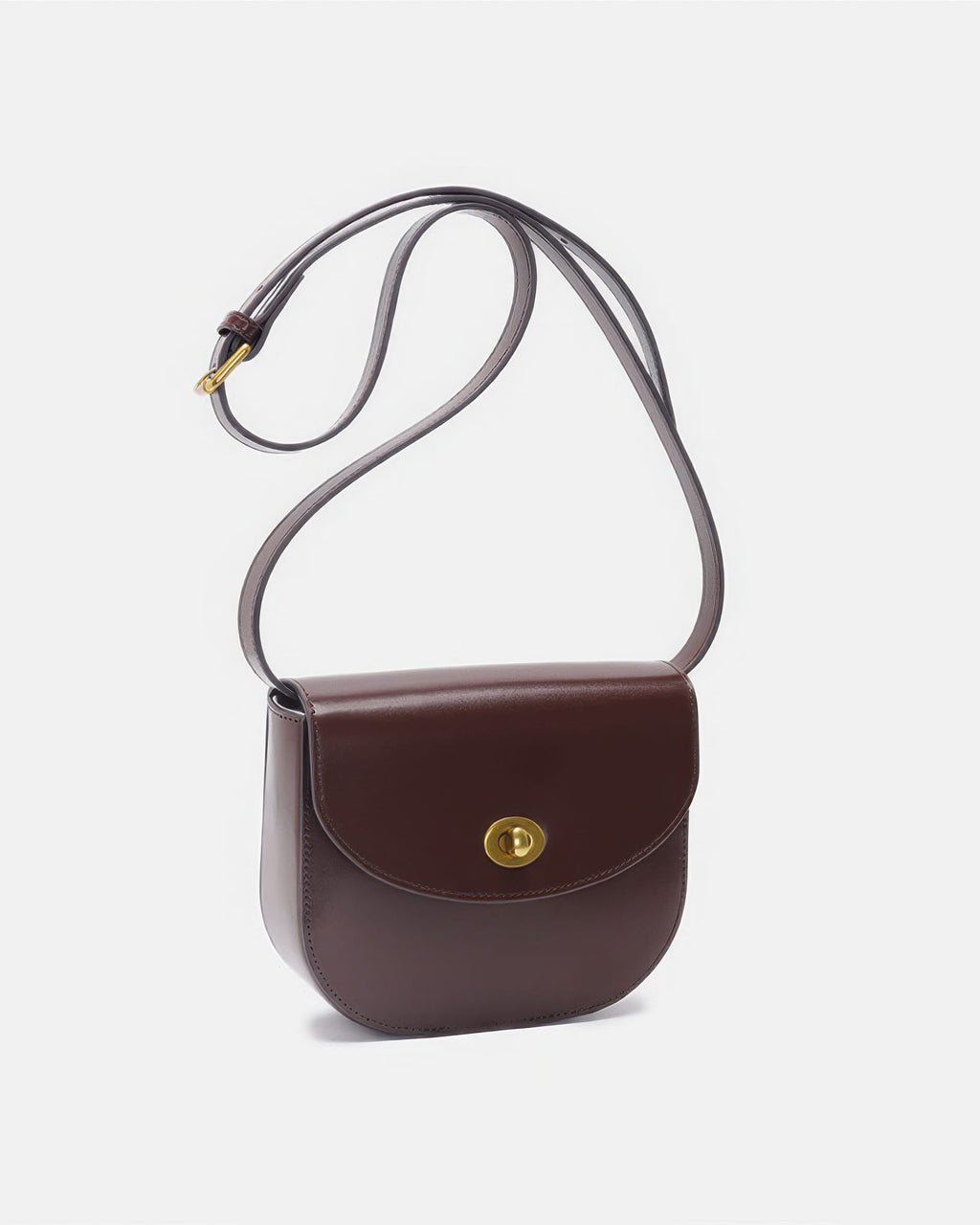Studio product shot of a dark brown classic leather flap saddle crossbody bag with a long strap and gold hardware.