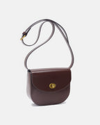 Studio product shot of a dark brown classic leather flap saddle crossbody bag with a long strap and gold hardware.