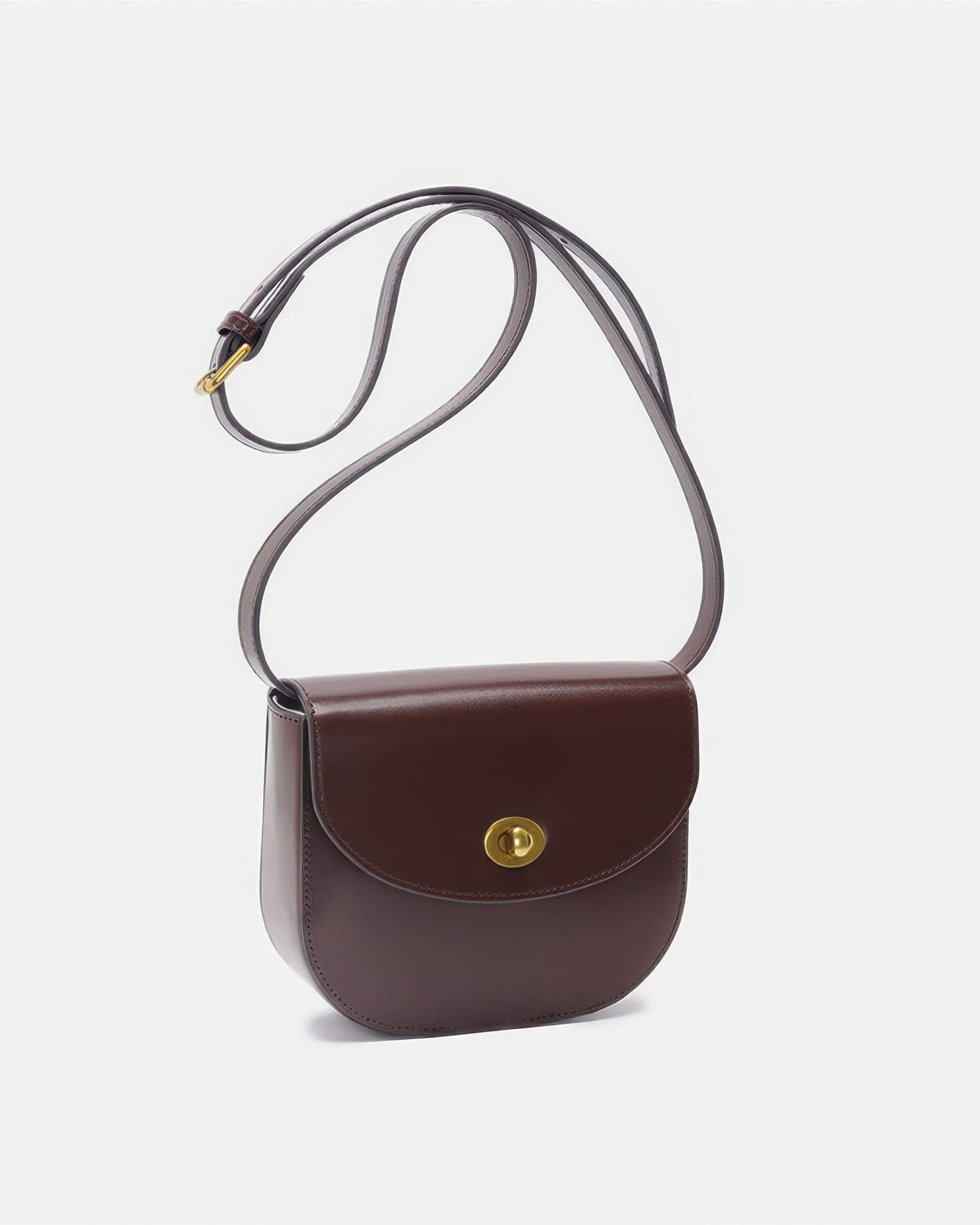 Studio product shot of a dark brown classic leather flap saddle crossbody bag with a long strap and gold hardware.
