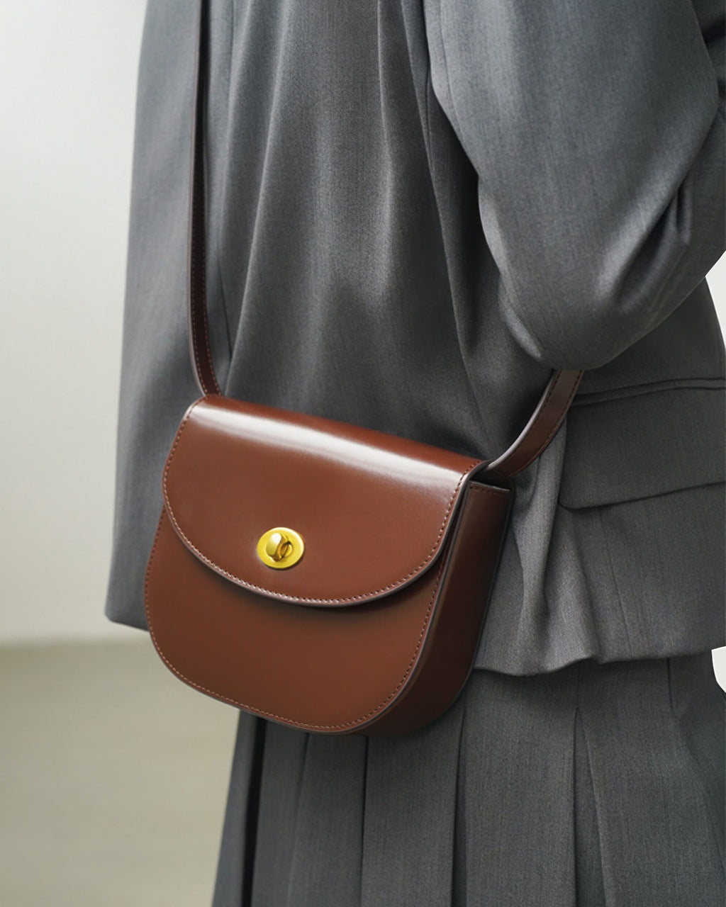 Side-back view of a brown classic leather flap saddle crossbody bag worn over a grey suit jacket.