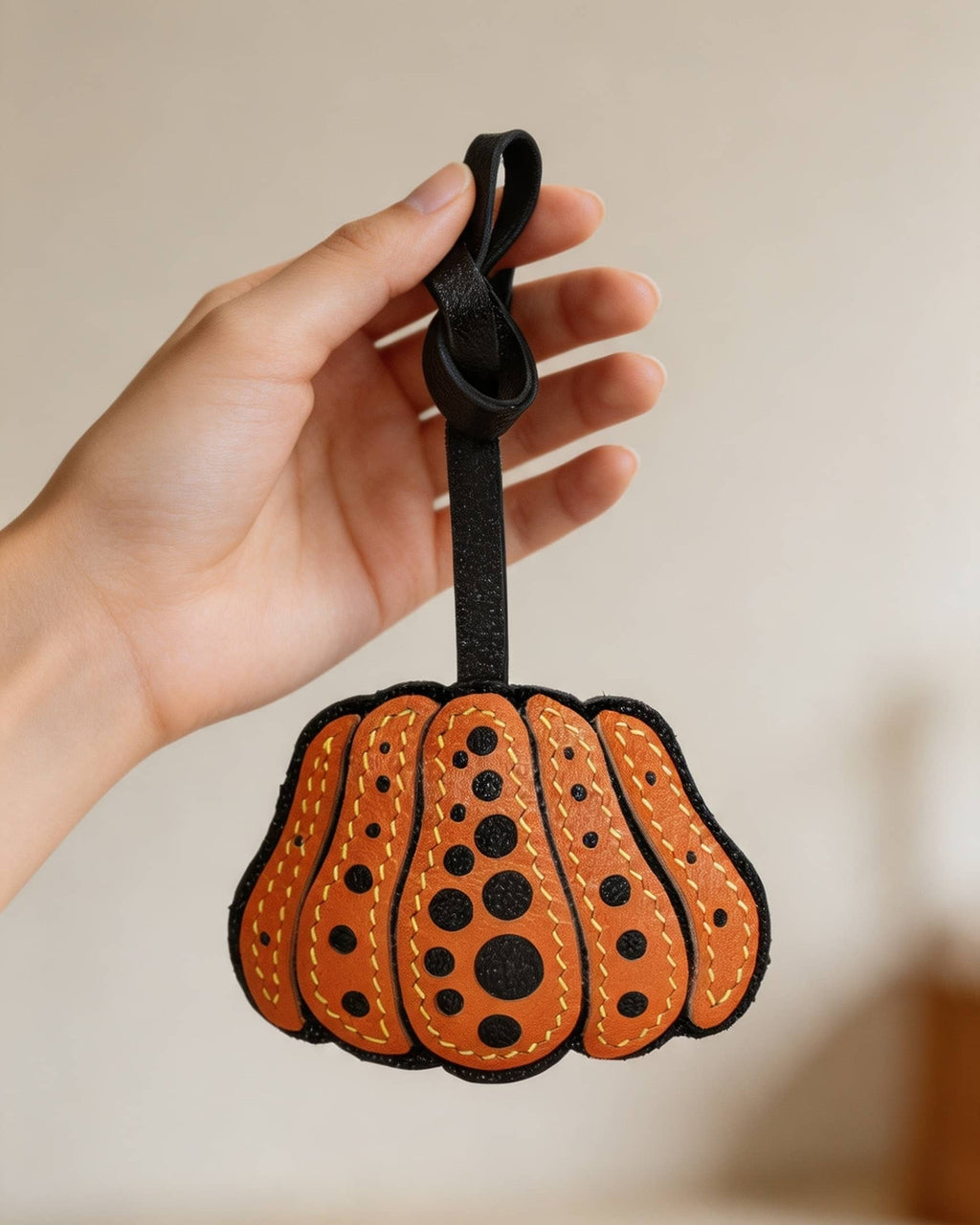 Hand holding an orange dotted pumpkin leather bag charm made of French goatskin.