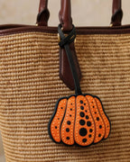 Close-up of orange and black polka dot pumpkin bag charm on a straw handbag.