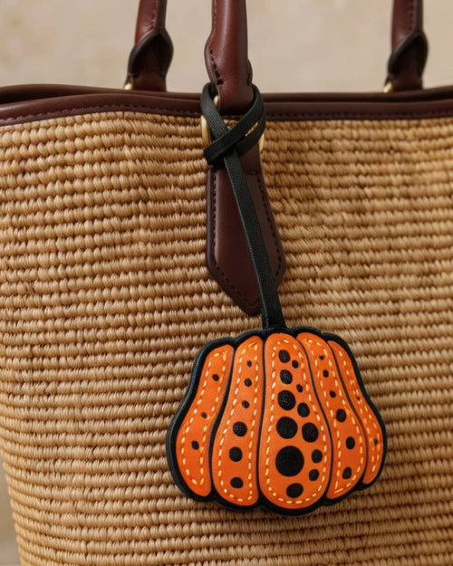 Close-up of orange and black polka dot pumpkin bag charm on a straw handbag.