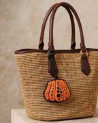 Woven tote bag styled with a decorative orange dotted pumpkin leather bag charm.