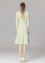 The back view of a model wearing a light green blazer dress, highlighting the fitted waist, mermaid-style skirt, and white high-heeled pumps.