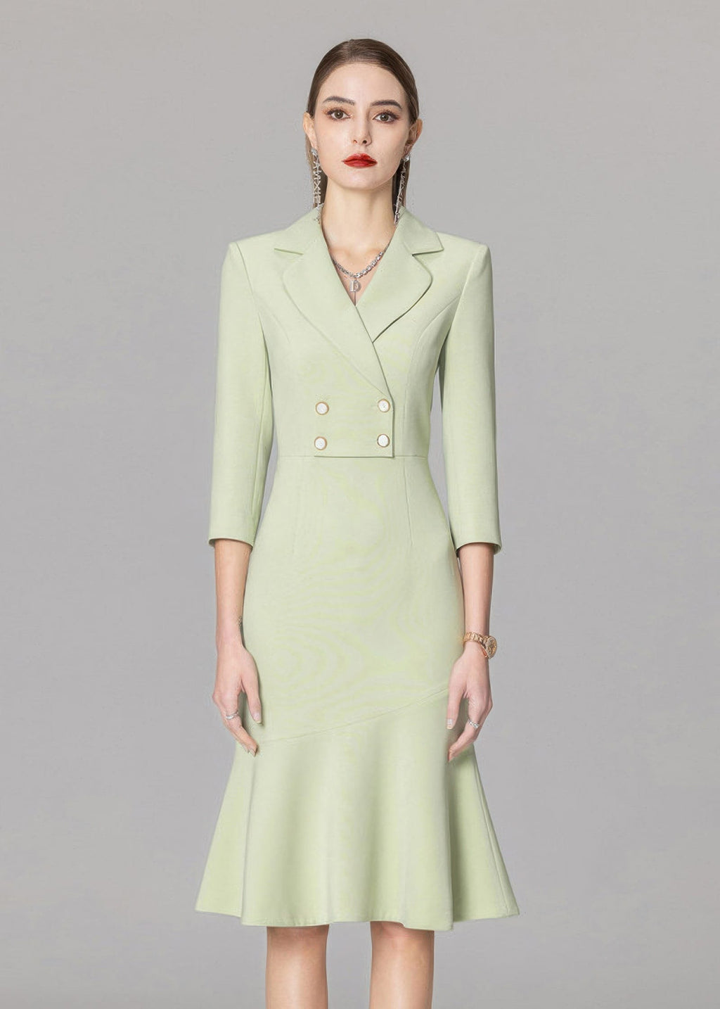 A medium-shot portrait of a model in a light green double-breasted blazer dress featuring four gold-rimmed buttons and a notched lapel.