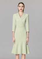A medium-shot portrait of a model in a light green double-breasted blazer dress featuring four gold-rimmed buttons and a notched lapel.