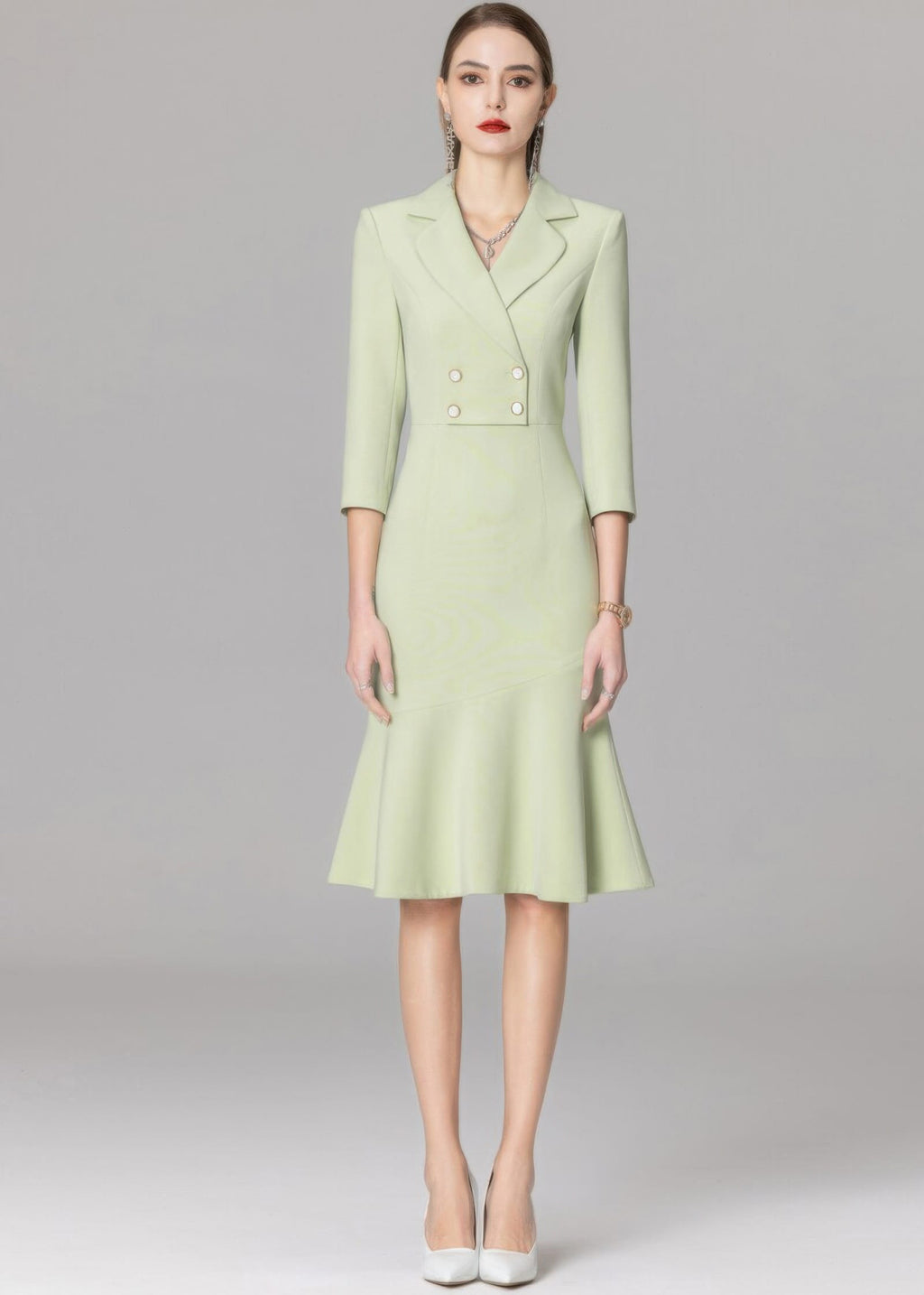 A full-length front view of a model in a mint green double-breasted blazer dress with white pointed-toe heels.