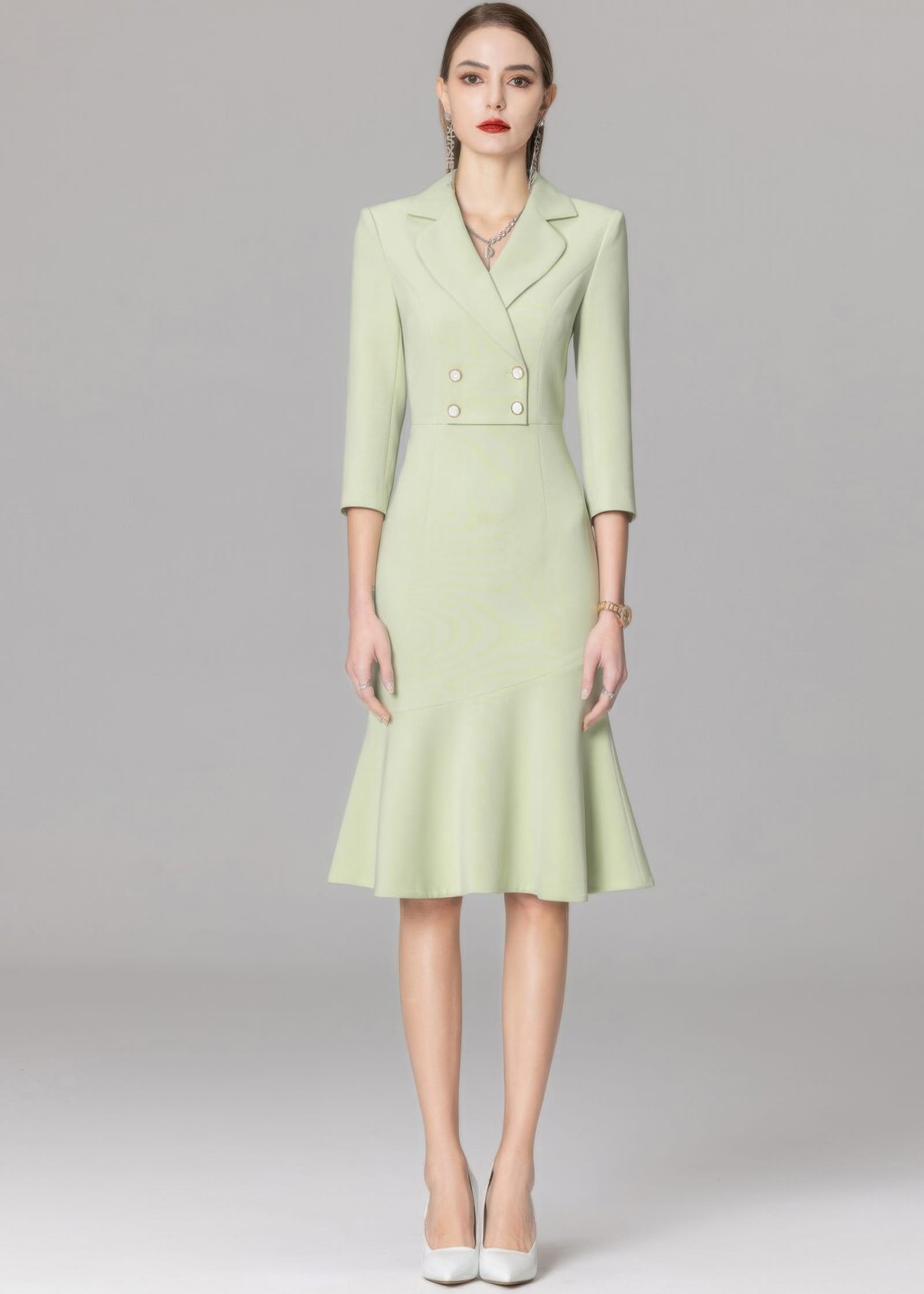 A full-length front view of a model in a mint green double-breasted blazer dress with white pointed-toe heels.
