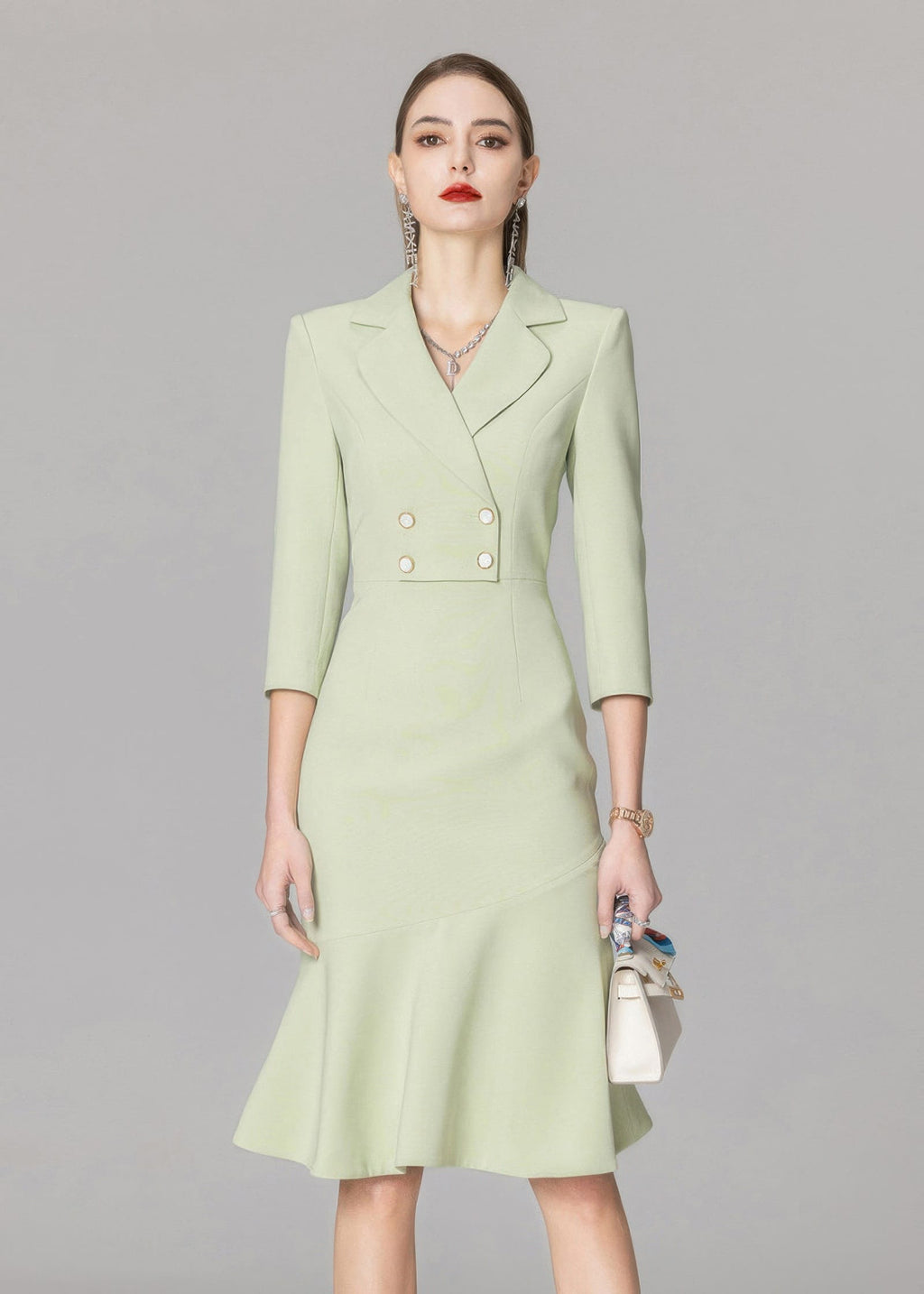 A centered front view of the model in the light green blazer dress, accessorized with a watch, necklace, and small white bag.