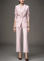 A woman wearing a light pink, double-breasted tailored pant suit with gold buttons and dark red heels.