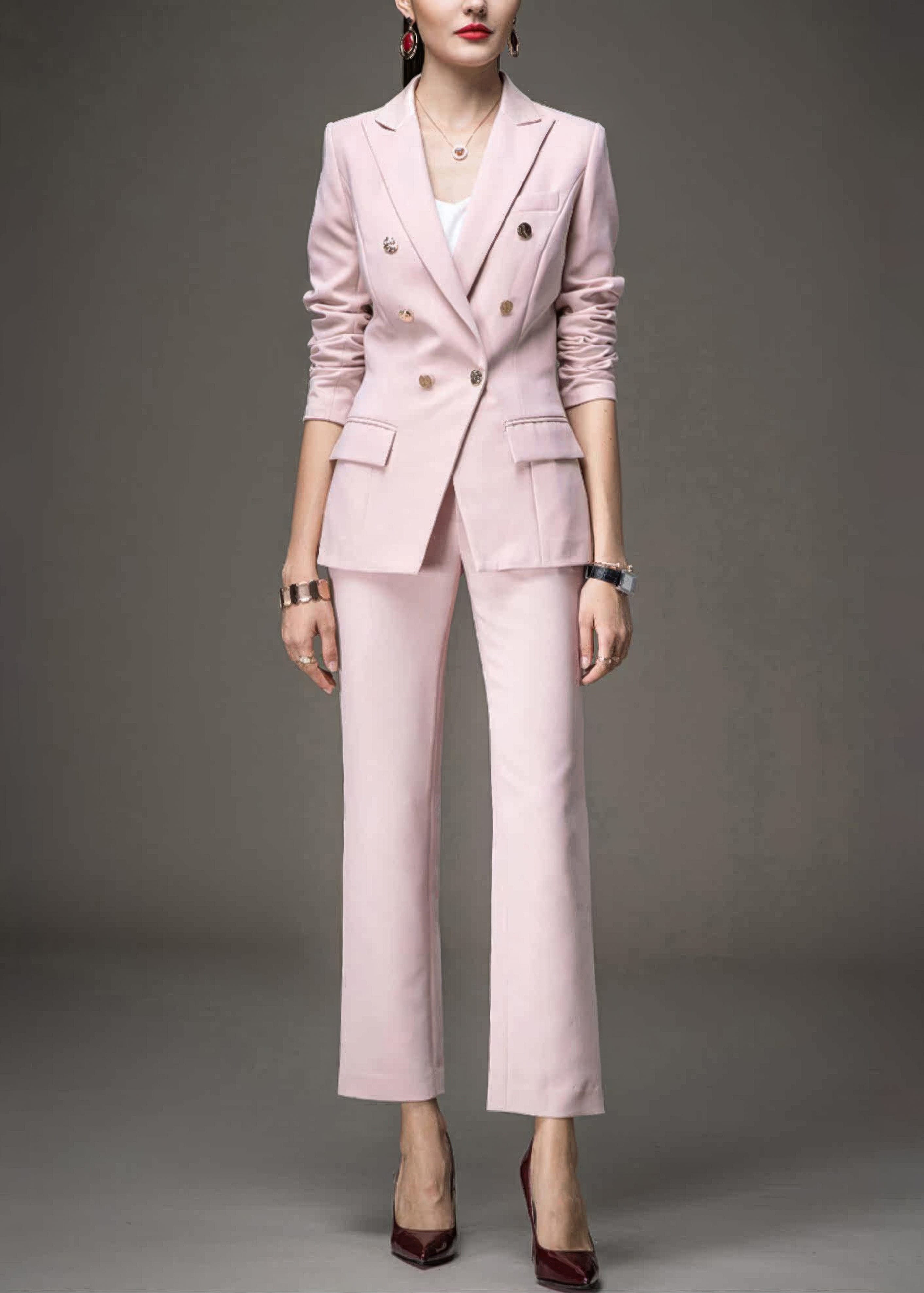 A woman wearing a light pink, double-breasted tailored pant suit with gold buttons and dark red heels.