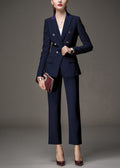 A woman posing in a navy blue tailored pant suit, holding a burgundy clutch bag.
