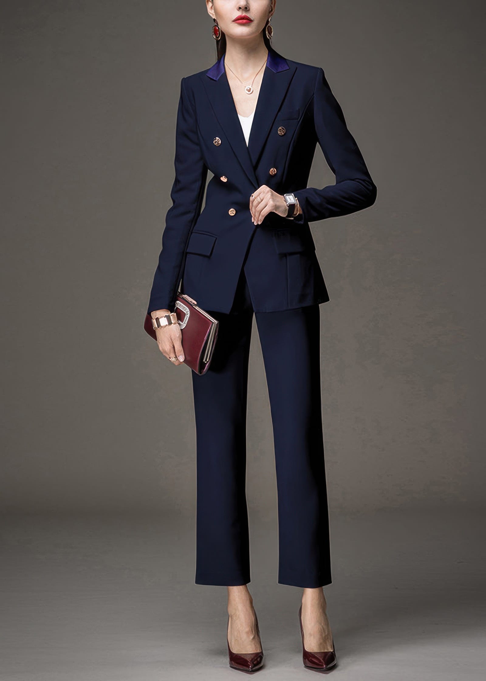A woman posing in a navy blue tailored pant suit, holding a burgundy clutch bag.