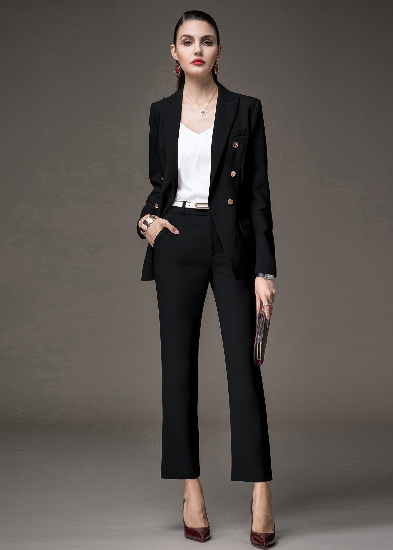 A woman wearing a black double-breasted pant suit with a white top, featuring one hand in her pocket.