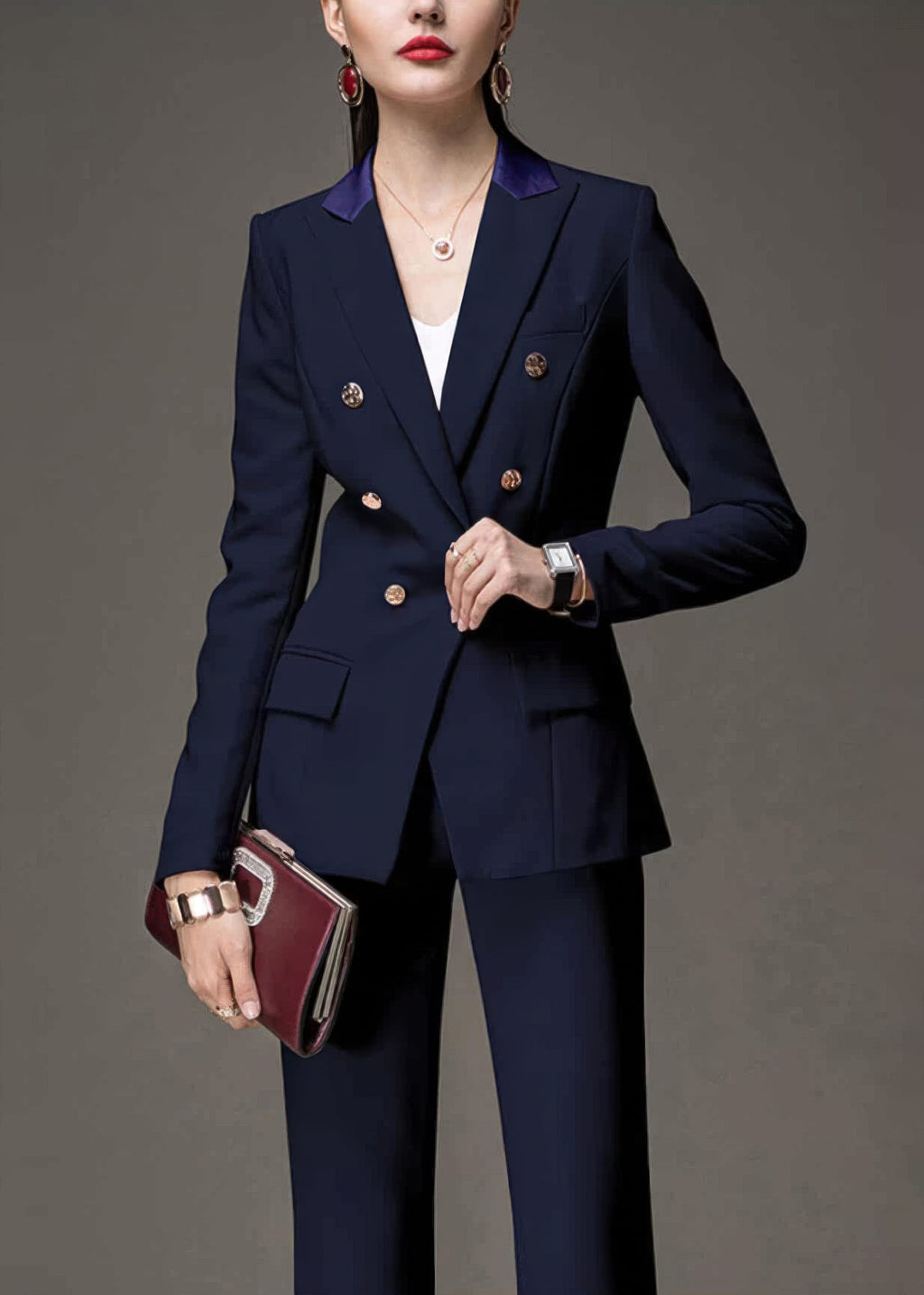 Three-quarter view of a woman in a navy blue tailored suit, accessorized with a watch and a burgundy clutch.