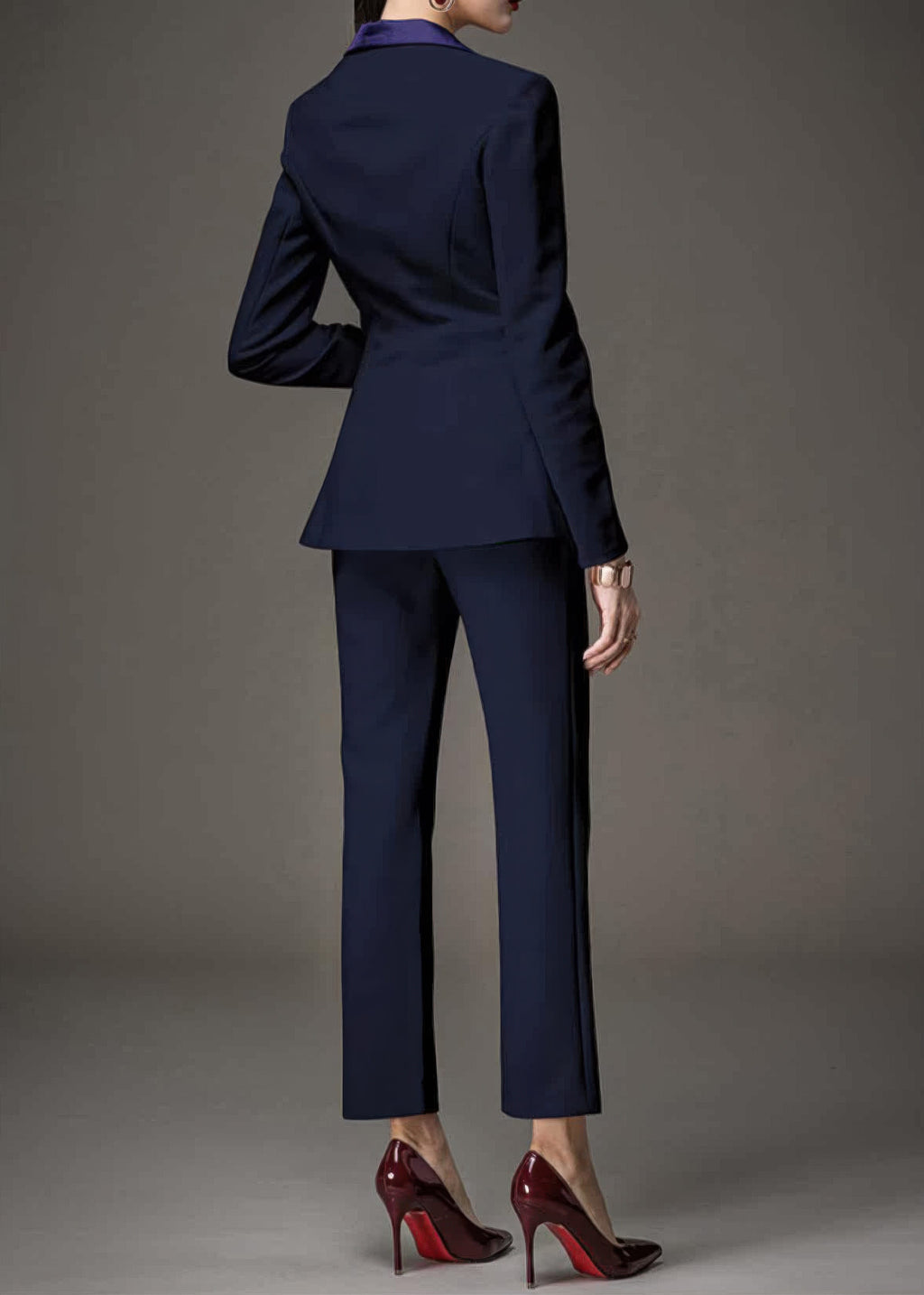 Back view of a woman wearing a navy blue tailored pant suit and high-heeled red-bottom shoes.