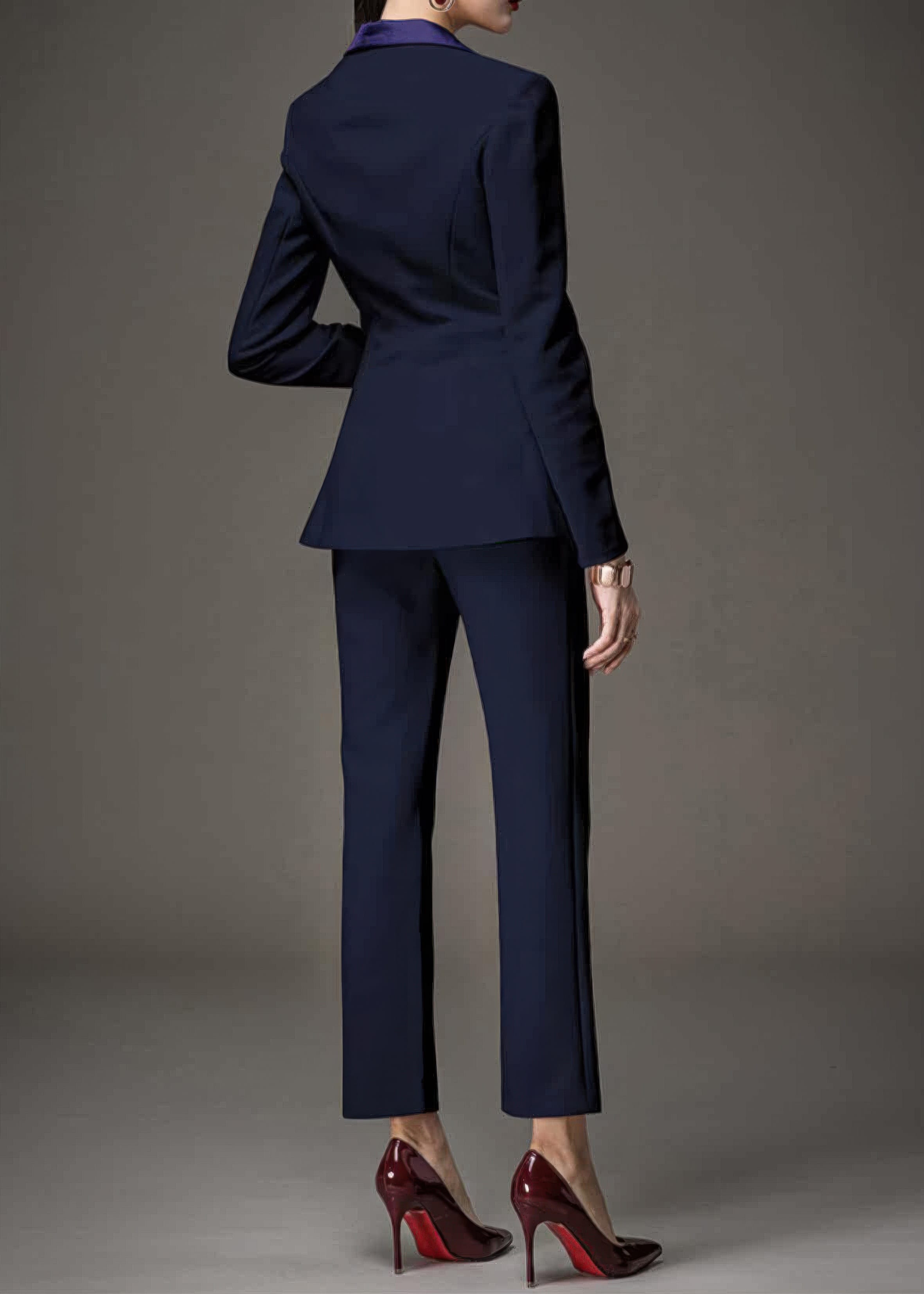 Back view of a woman wearing a navy blue tailored pant suit and high-heeled red-bottom shoes.