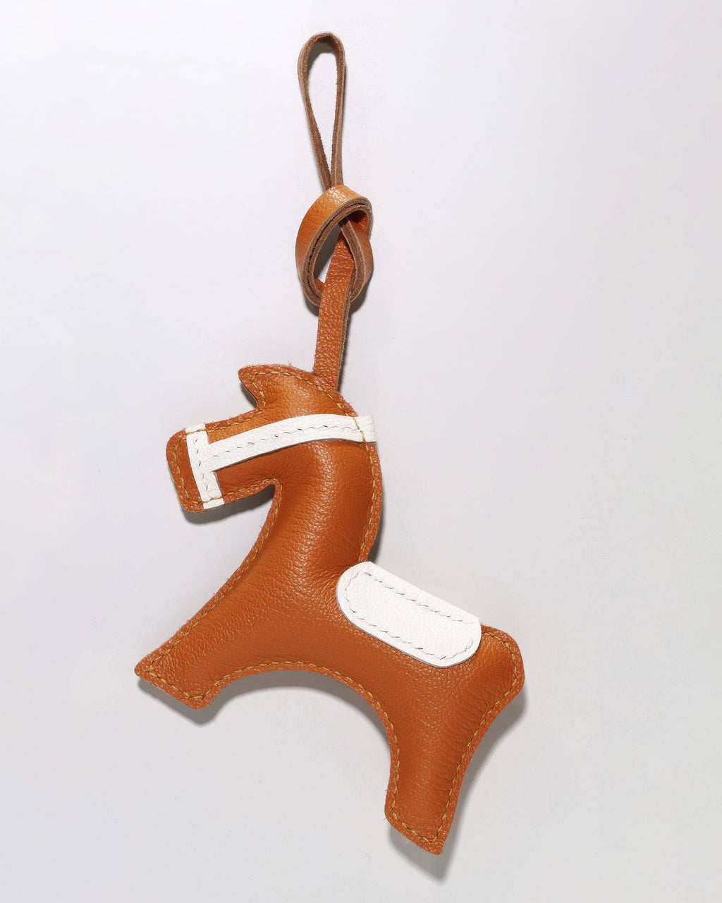 Front view of an equestrian horse bag charm in tan brown leather with a knotted leather strap for attachment.