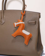 Close-up of an orange leather equestrian horse charm attached to a luxury taupe leather handbag.