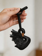 Hand holding a black swan leather bag charm made of textured French goatskin.