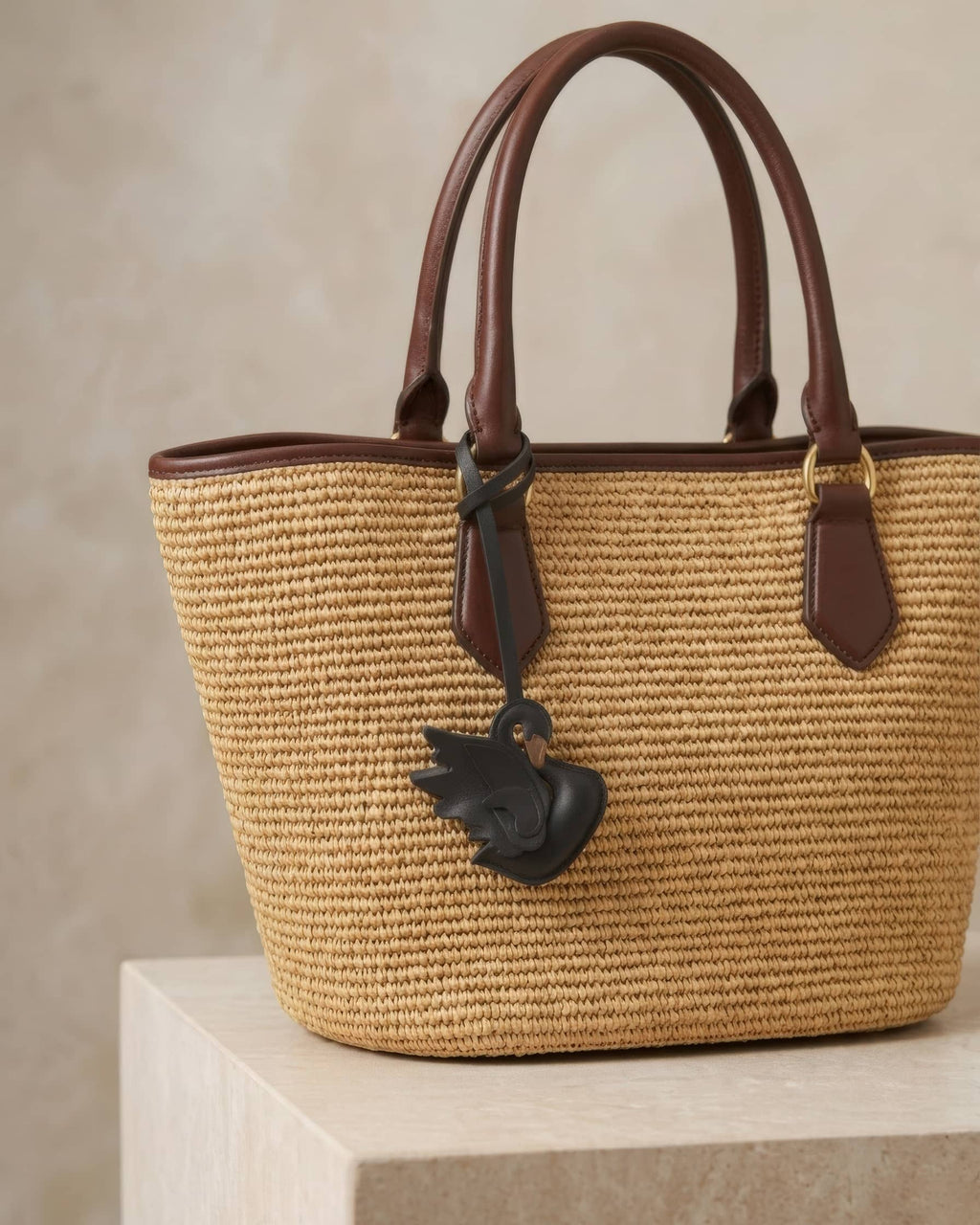 Graceful black swan leather bag charm attached to a woven straw tote bag handle.