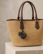 Graceful black swan leather bag charm attached to a woven straw tote bag handle.