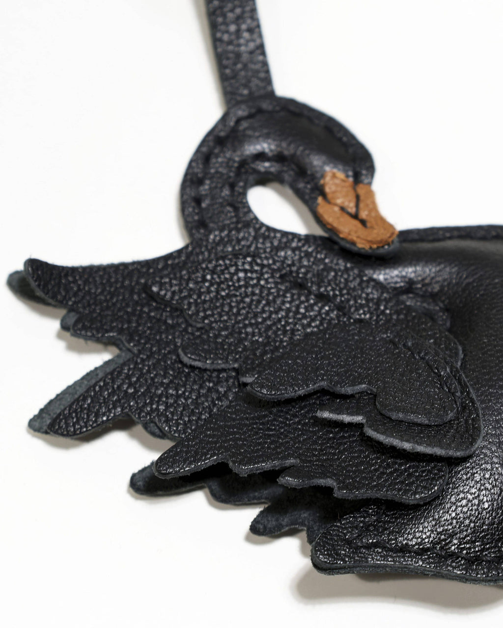 Extreme macro close-up of layered leather feathers, fine stitching, and French goatskin texture on a black swan bag charm.
