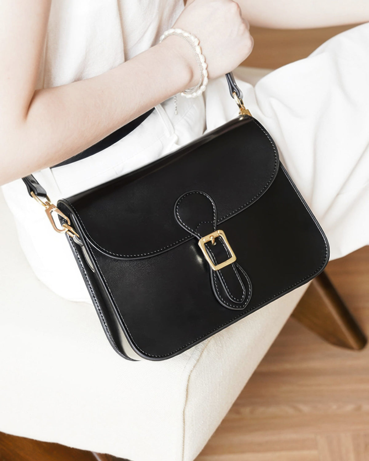 Close-up view of a black leather crossbody bag featuring a front flap and gold hardware buckle, held by a model.