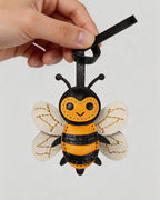 Hand holding a yellow and black handcrafted honeybee leather bag charm with white stitched wings.