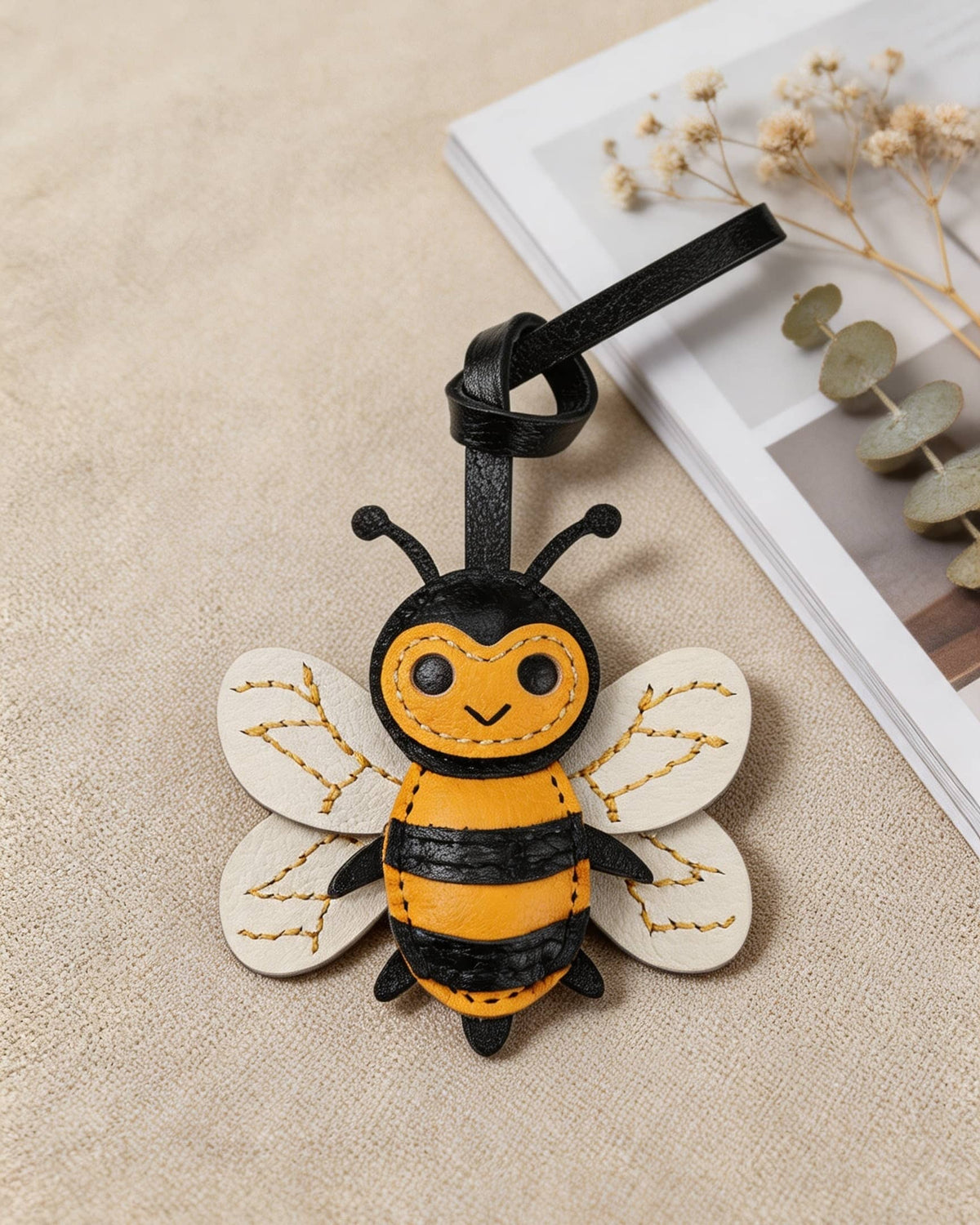 Honeybee goatskin leather bag charm laid flat next to dried flowers on a neutral surface.