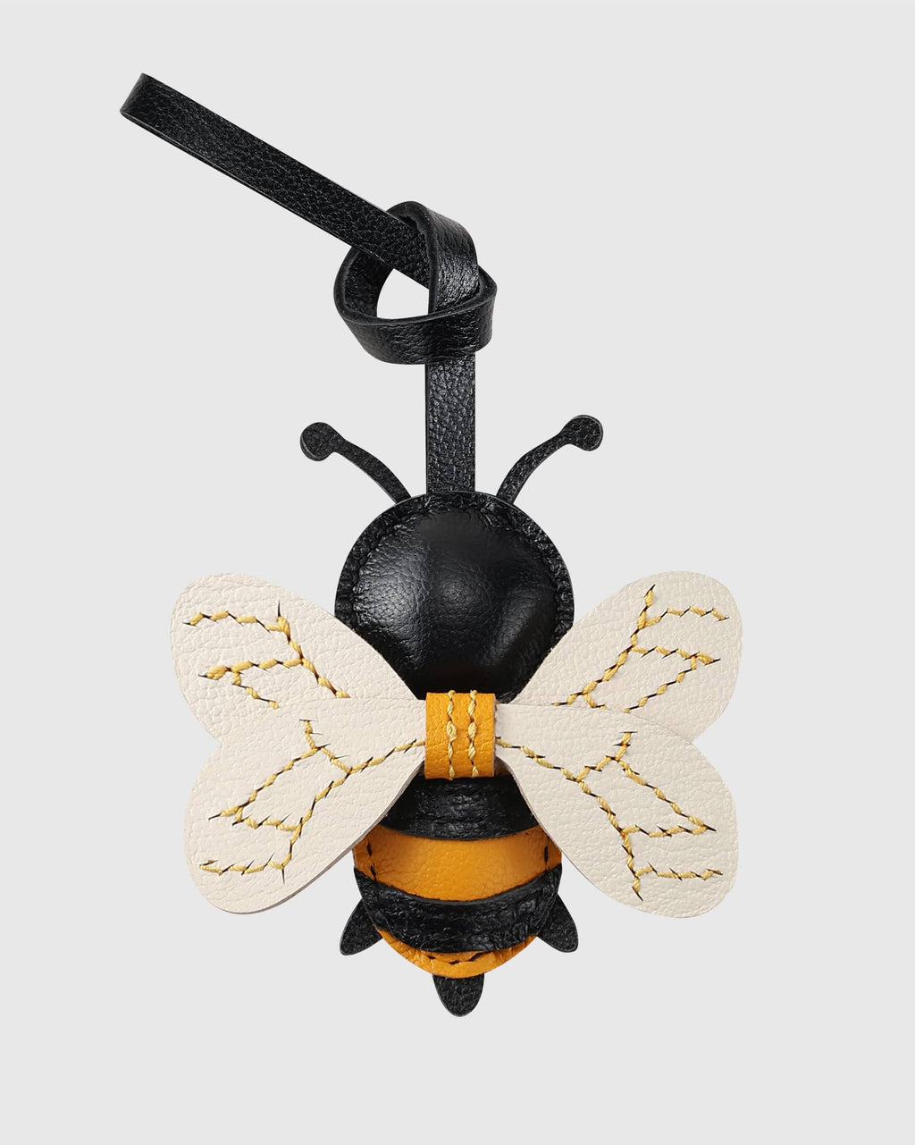 Back view of a honeybee leather bag charm showing yellow stitching on white leather wings and black body.