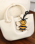 Cream white leather handbag styled with a yellow and black honeybee charm accessory.