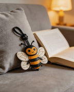 Honeybee leather charm resting on a grey sofa next to an open book in a cozy setting.