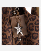 Close-up macro view of silver star charm and brown leather tag accent on leopard print suede purse