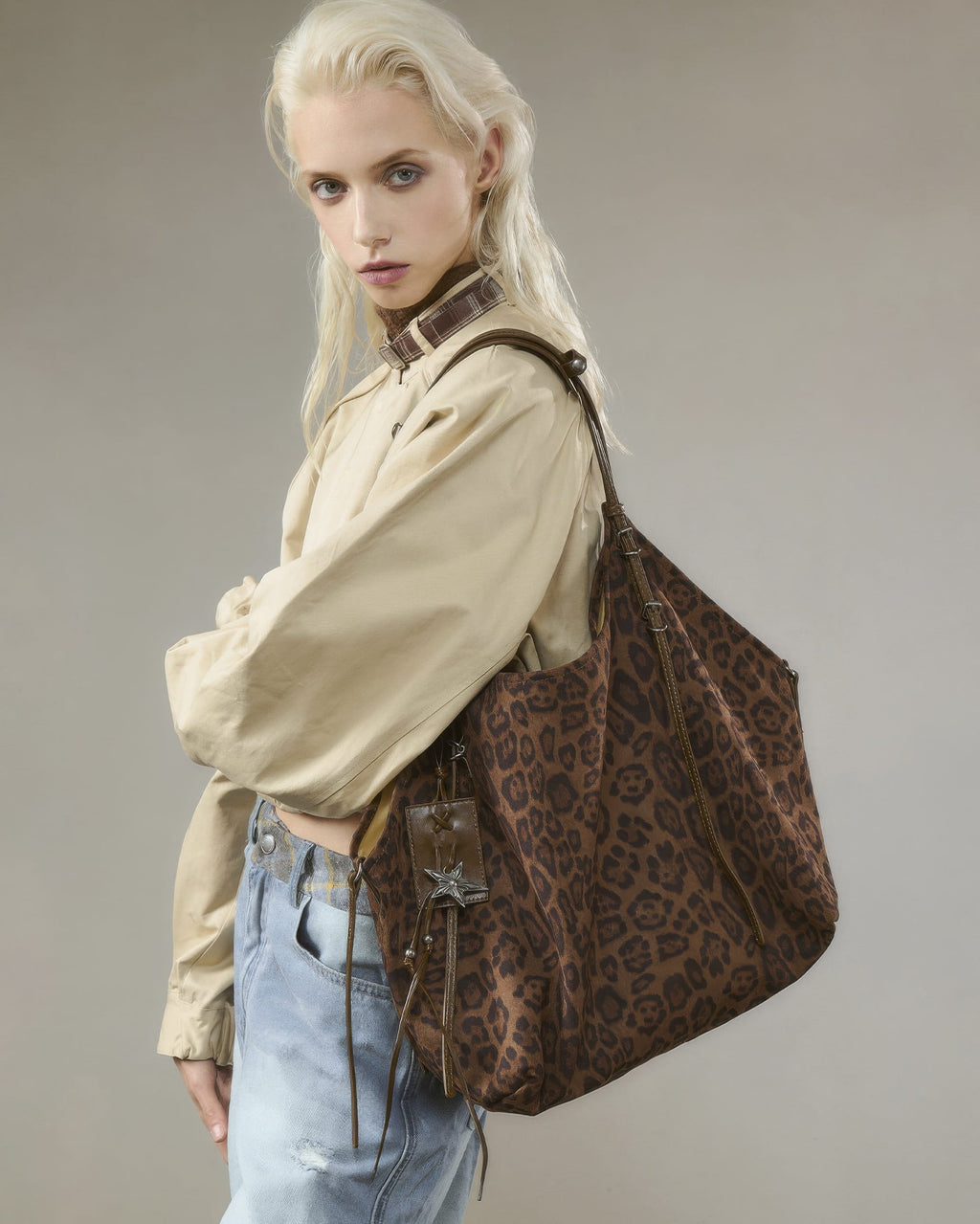 Blonde model carrying a large brown leopard print faux suede shoulder bag with star charm and strap details