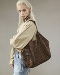 Blonde model carrying a large brown leopard print faux suede shoulder bag with star charm and strap details