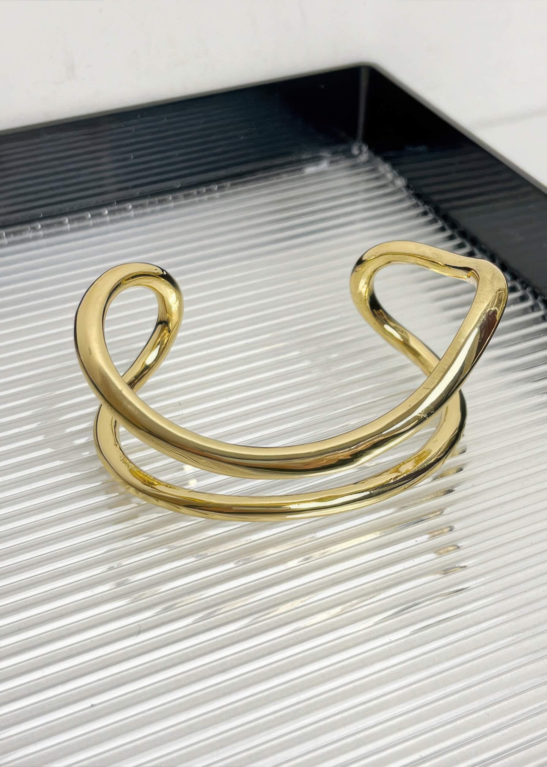 A single gold-tone fluid wave statement bangle showcasing its open-cuff design and smooth, curved lines.