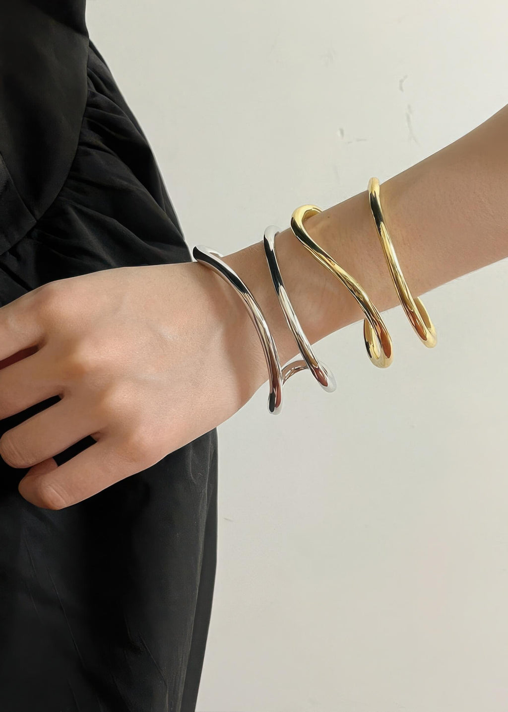 Stylized shot of a model wearing both silver and gold fluid wave bangles together for a mixed-metal stacked look.