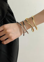 Stylized shot of a model wearing both silver and gold fluid wave bangles together for a mixed-metal stacked look.