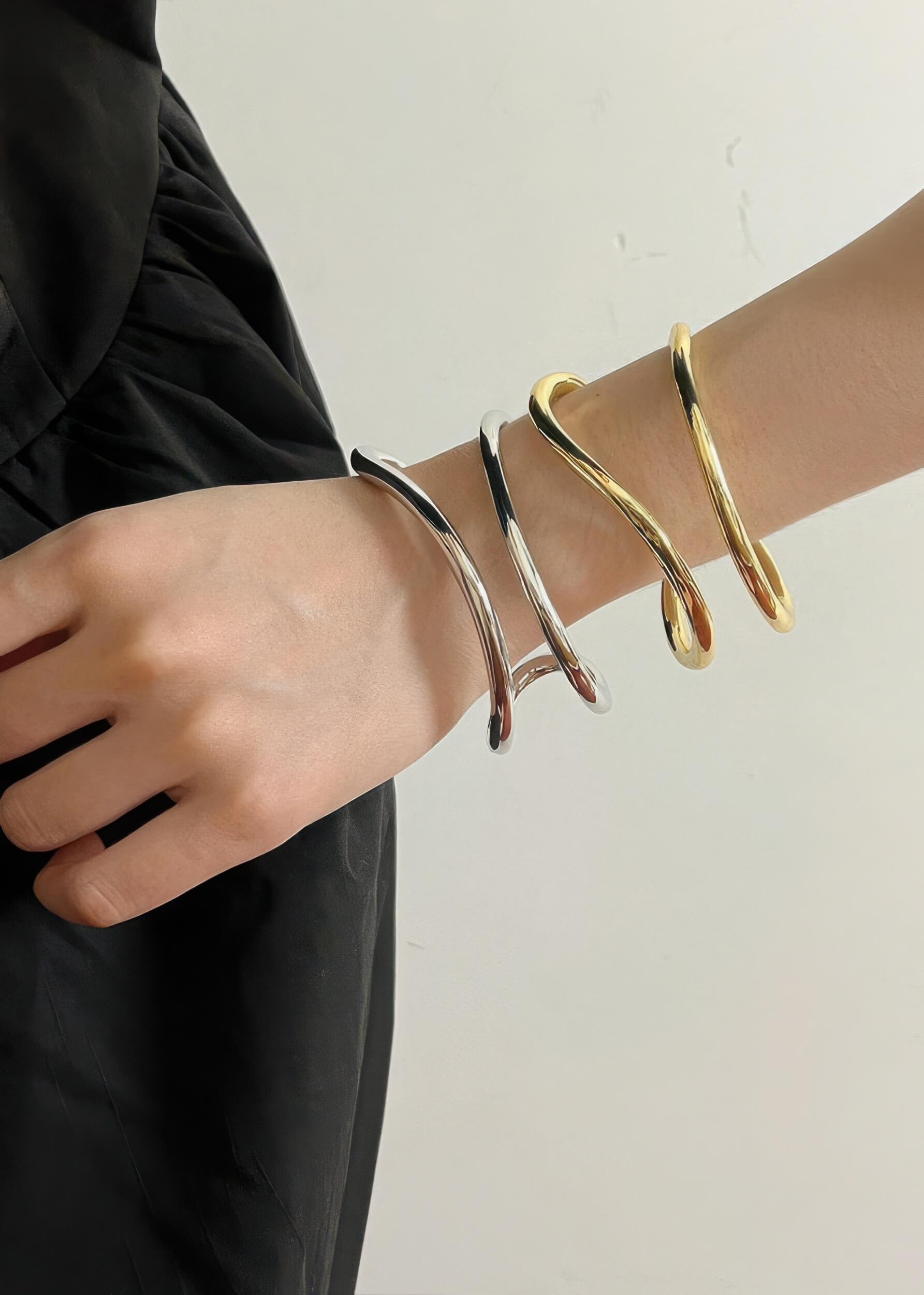 Stylized shot of a model wearing both silver and gold fluid wave bangles together for a mixed-metal stacked look.