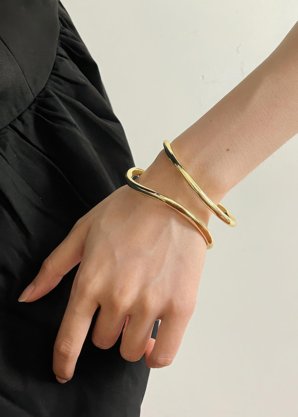 Side view of the gold fluid wave bangle on a wrist, highlighting its organic, wavy shape and metallic luster.
