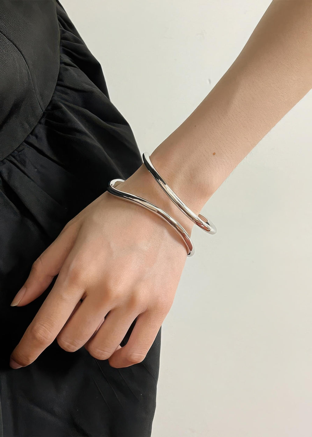 Side view of the silver fluid wave statement bangle on a wrist, showing the elegant gap and wrap-around style.