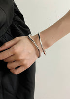 High-shine silver wave-shaped metal bangle worn on a person's wrist, featuring a modern, fluid silhouette.
