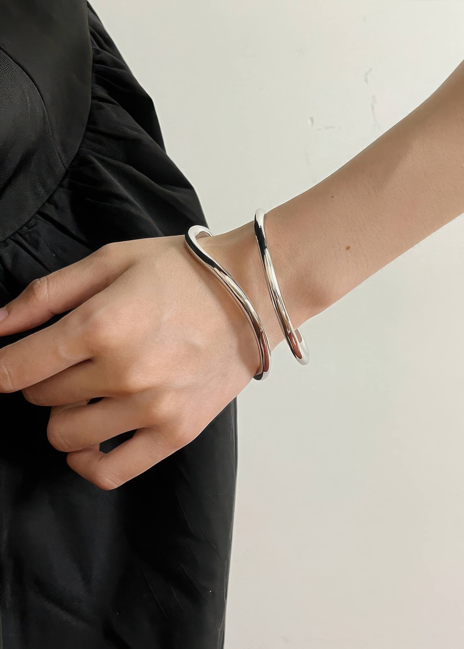 High-shine silver wave-shaped metal bangle worn on a person's wrist, featuring a modern, fluid silhouette.