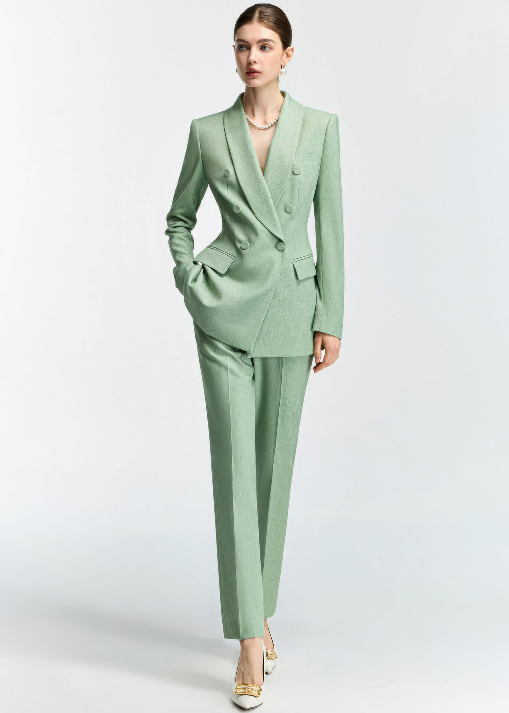 A dynamic full-length shot of the model posing with one hand in her pocket, showcasing the tailored silhouette of the mint green pantsuit.