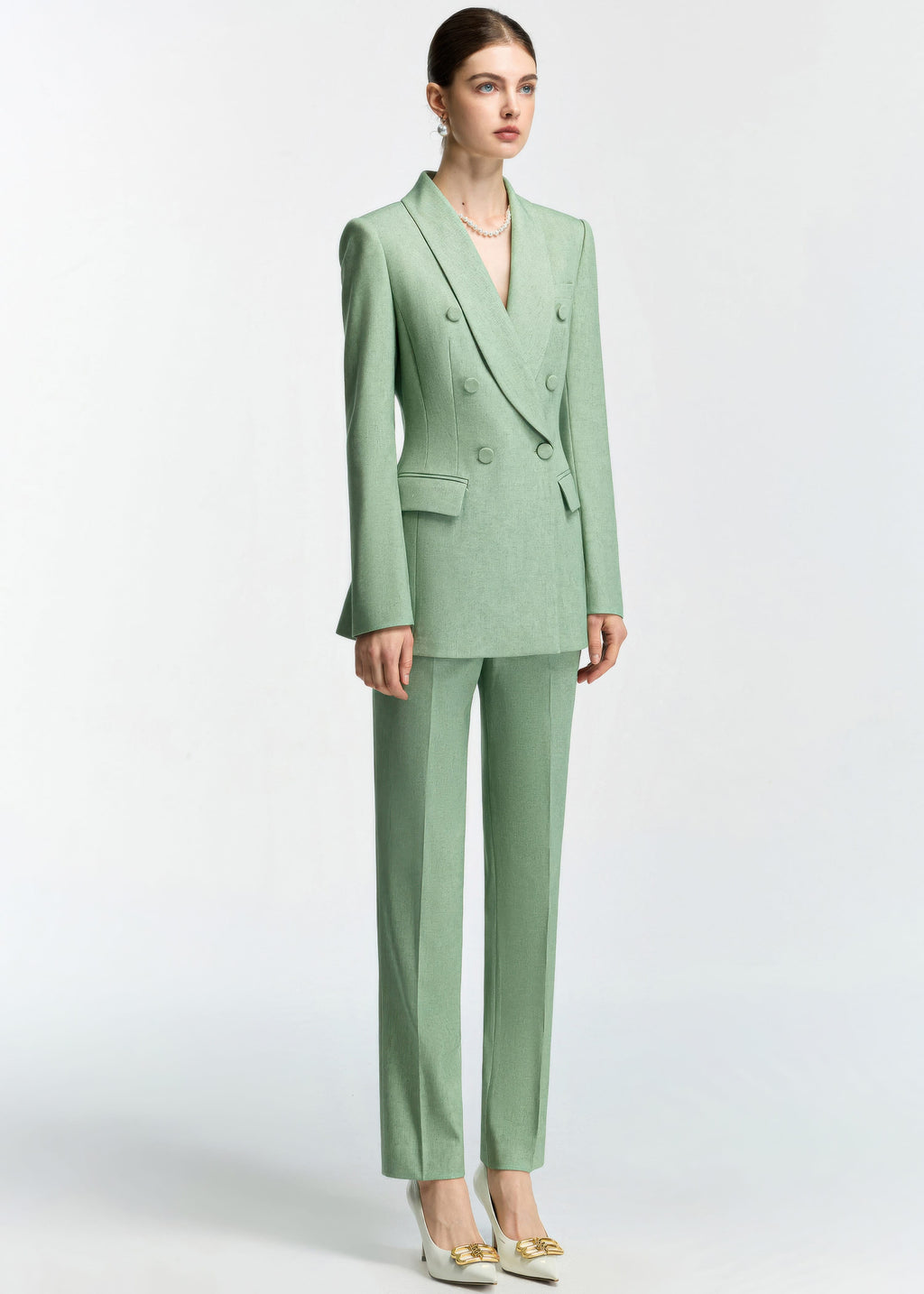 A full-length three-quarter view of the model standing, emphasizing the clean lines and structured shoulders of the mint green blazer.